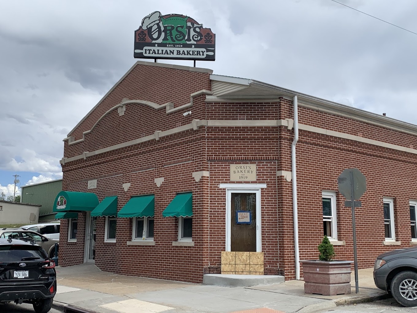 An outside view of a pizza shop, a red brick building with green awnings above all the windows