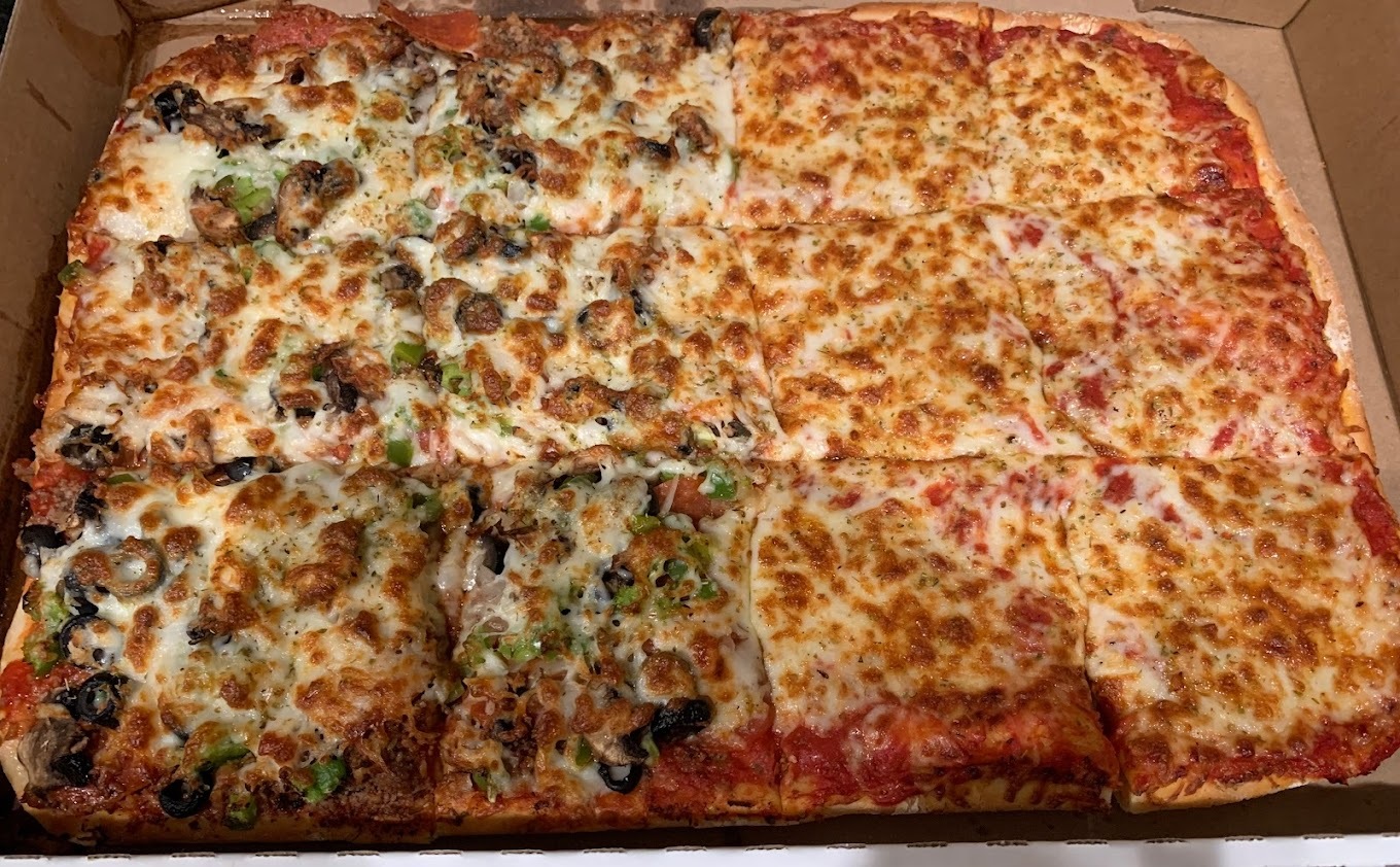 A view of a pizza, one side is veggies and the other is cheese, cut in rectangular shapes.