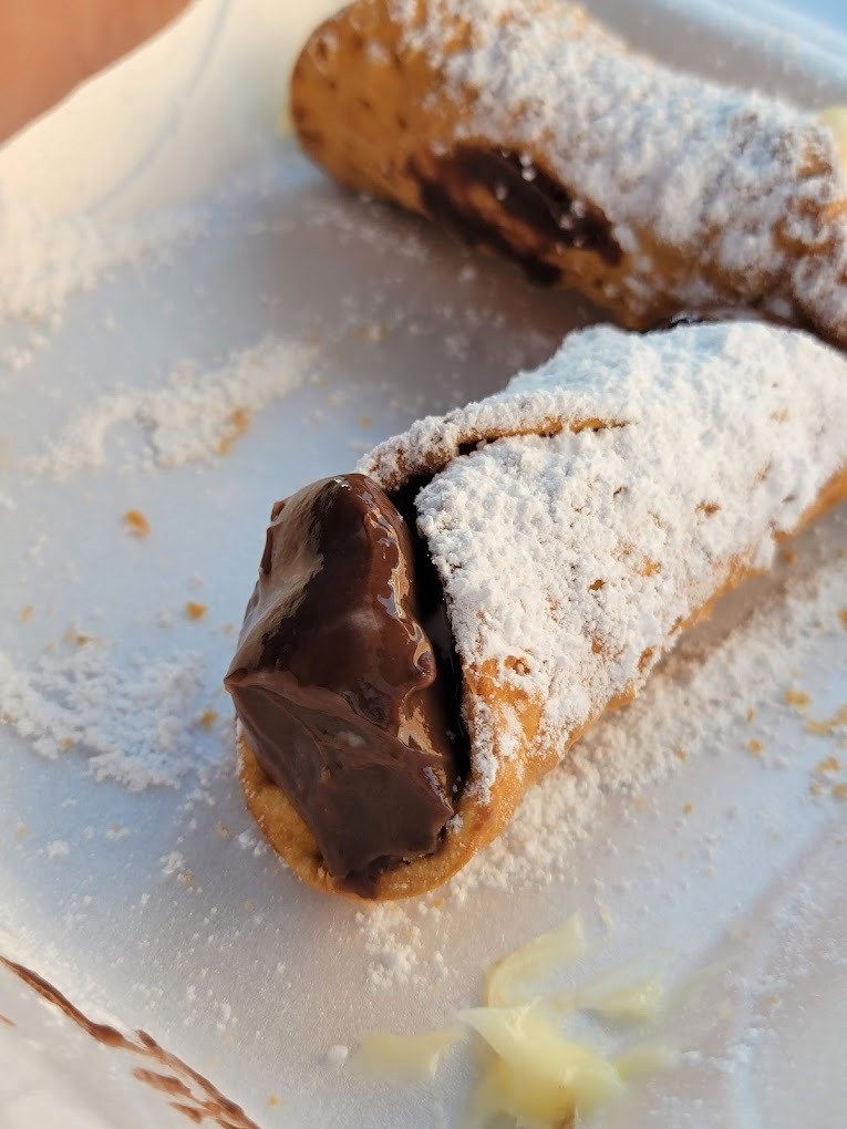 A white plate consisting of a cannoli stuffed with chocolate and topped with powdered sugar.
