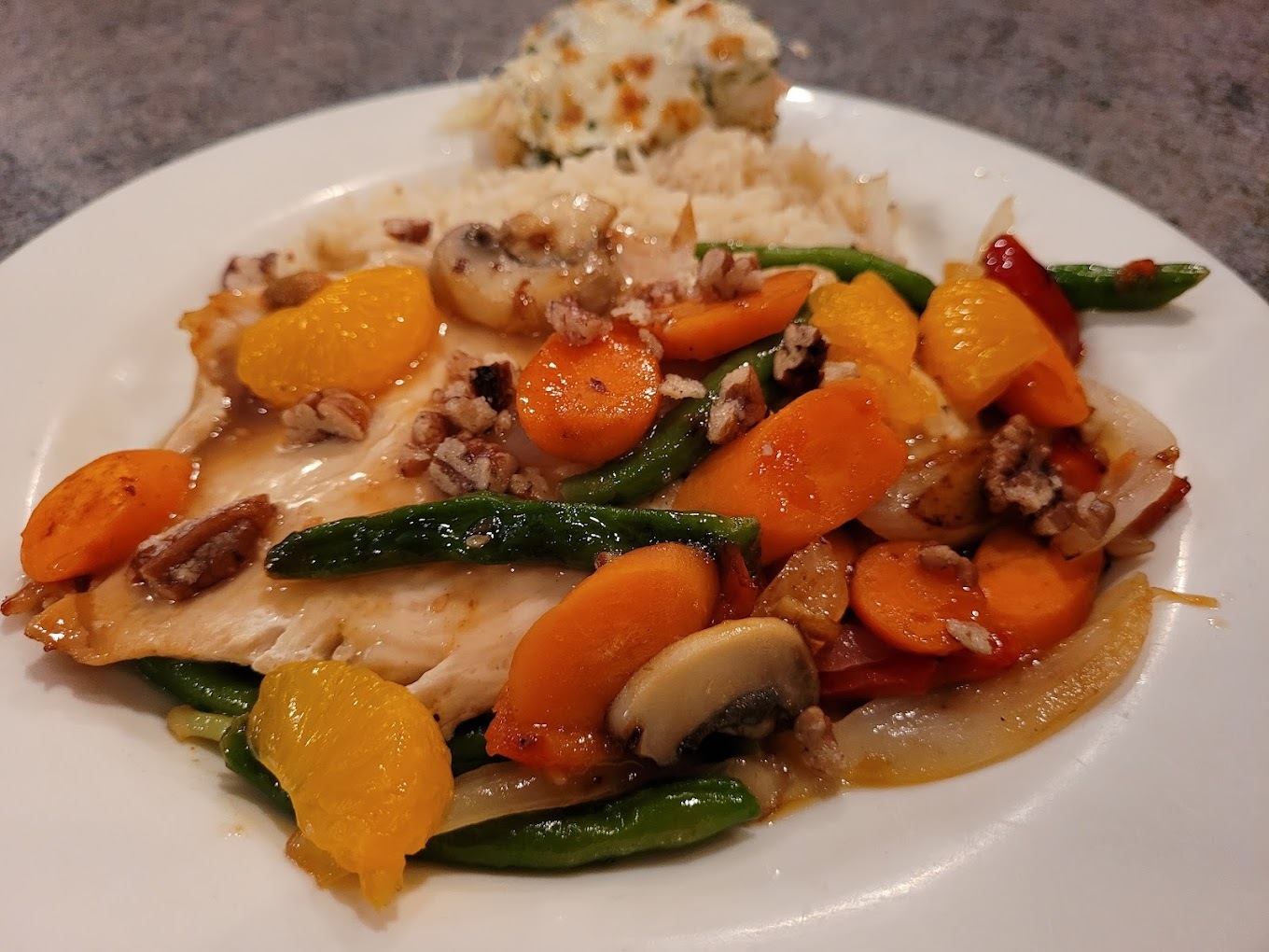 A white plate consisting of chicken topped with green beans, carrots, mushrooms, and mandarin oranges.