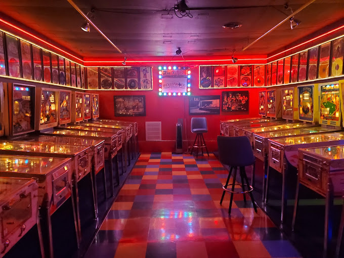 An inside view of an arcade with dark pink and red lights lining the walls, pinball arcade games are lining the walls.