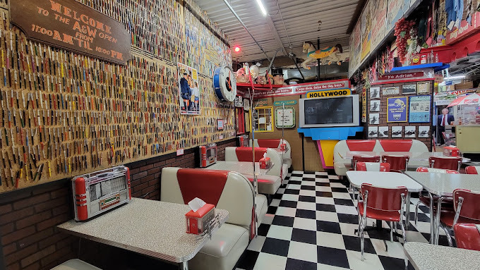 An inside view of an old school themed diner with checkered floors, and bright red and white themed booths, tables and chairs, and napkin dispensers.