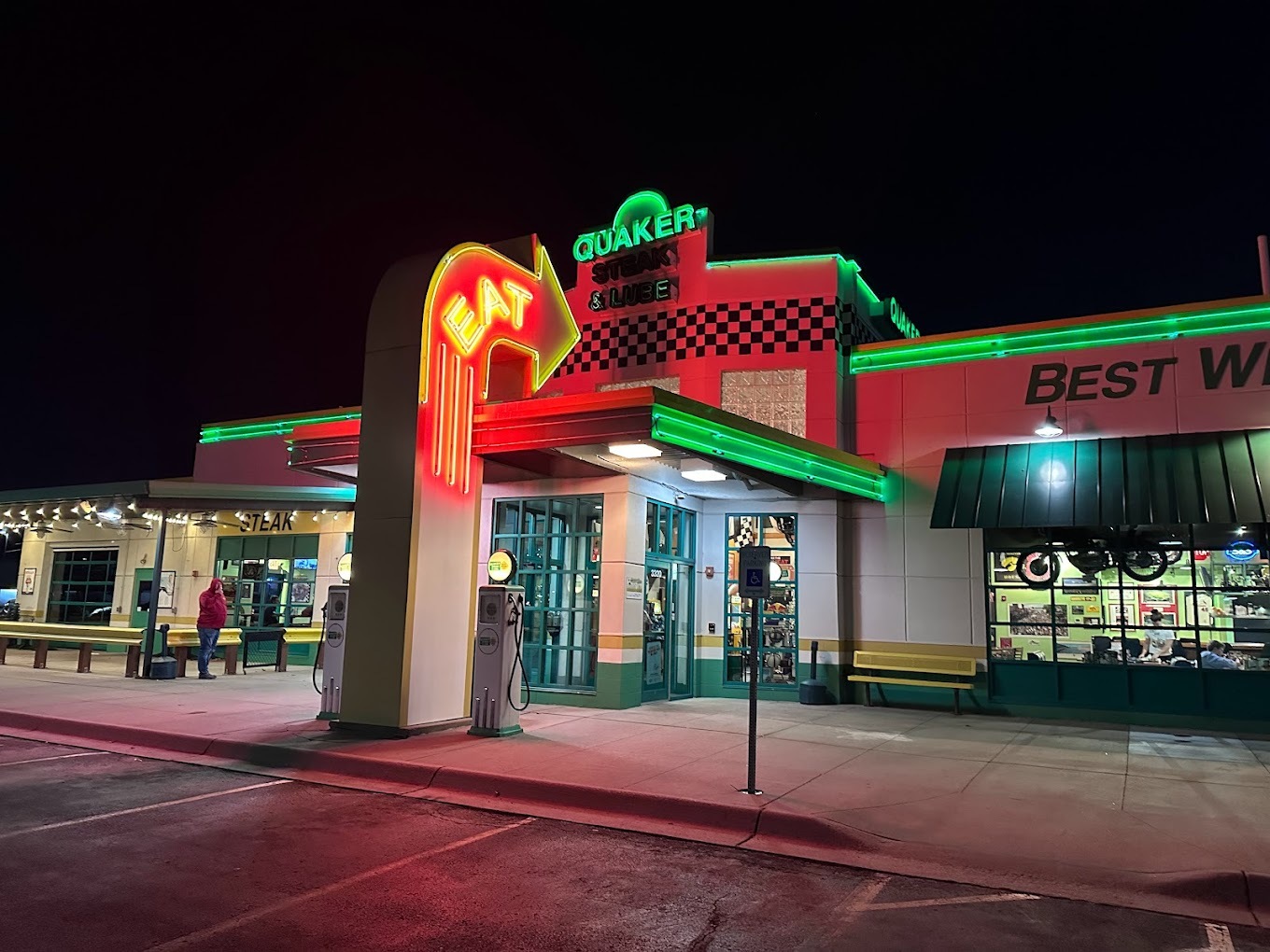An outside view of a restaurant with neon lights and a large arrow shaped sign pointing towards the building.