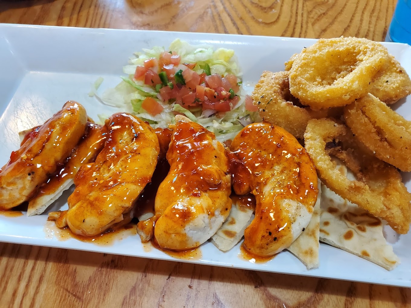 A white plate consisting of onion rings, lettuce, and pot stickers topped with an orange sauce.