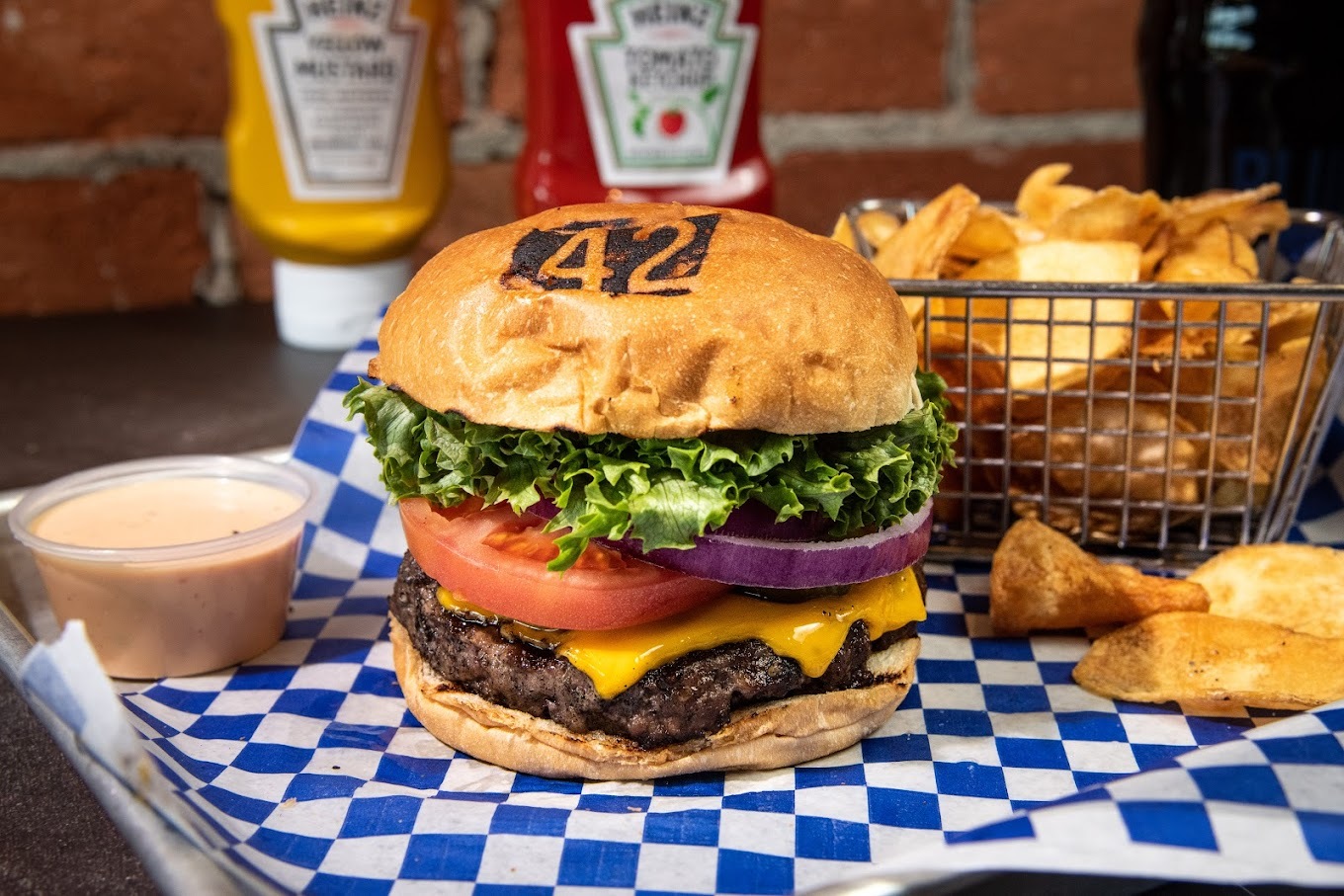 A serving tray loaded with a large burger, a large side of chips in a fryer basket and a side of sauce.
