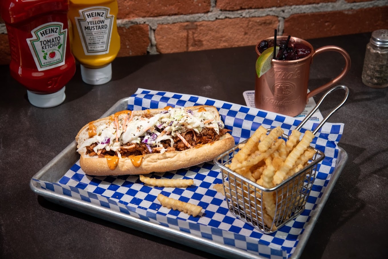A serving tray with blue checkered paper, serving a chili dog topped with coleslaw and a side of fries.