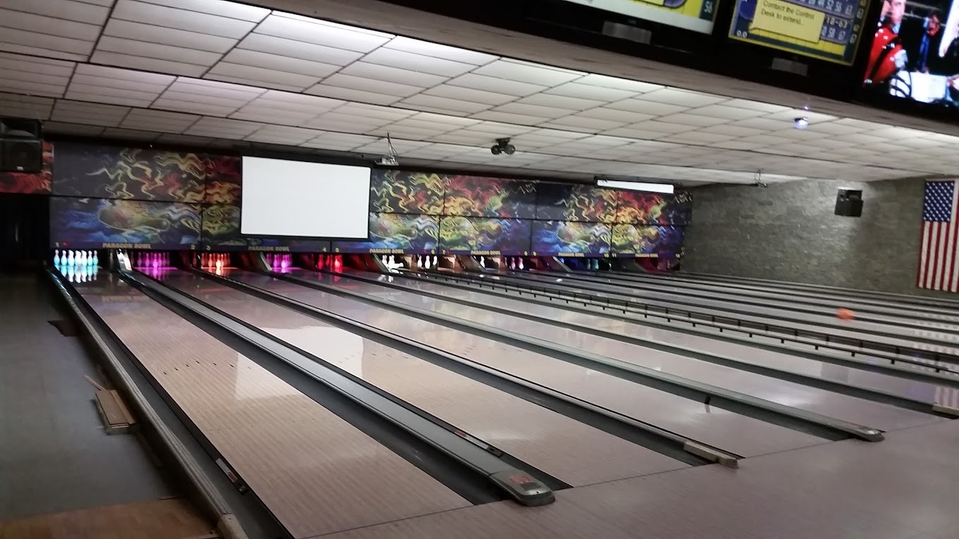 A view of bowling alley lanes, a white ceiling and the back wall is painted in all kinds of colors.