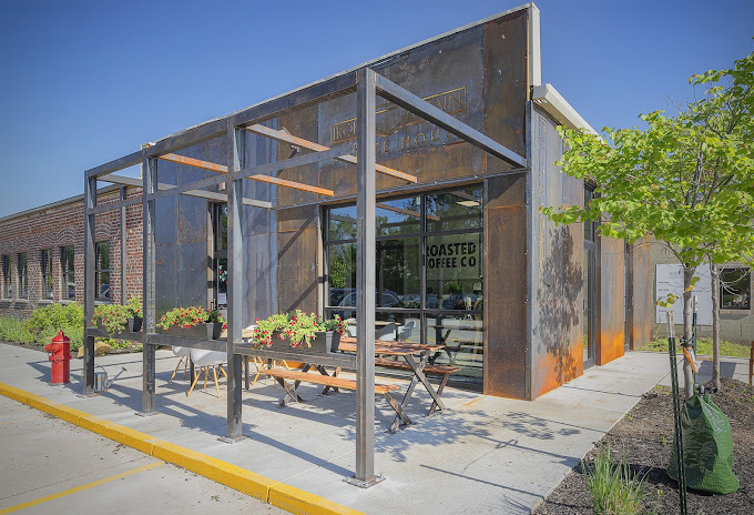 Exterior corner view of a cement and metal building with outdoor picnic tables.
