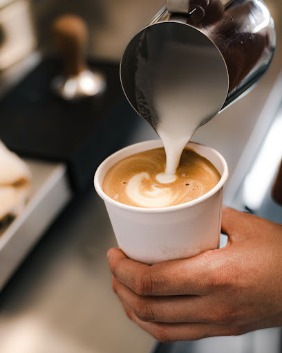 Close view of a person holding a coffee cup and pouring steamed milk into it.
