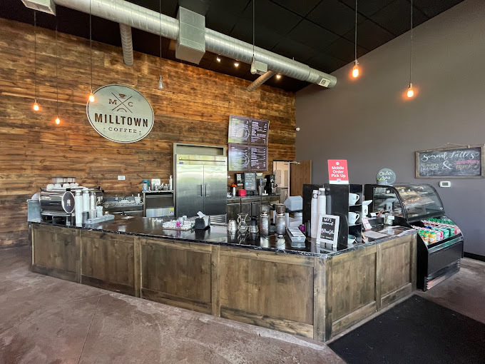 Interior view of a building with a wooden accent wall and a beige colored wall. The center of the room has the coffee making center and cash register.