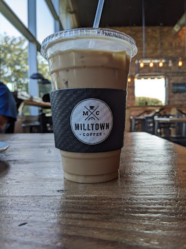 Close view of an iced coffee with a straw. Paper sleeve shows the Milltown Coffee logo.
