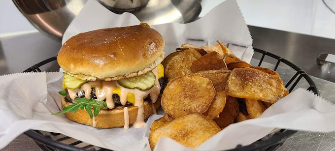 Close view of a cheesy burger and crispy fries on parchment in a black wire basket.