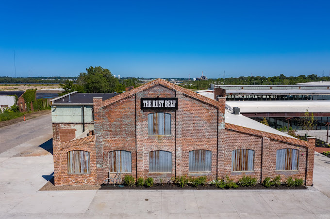 Faraway and overhead exterior view of a brick and steel building. Sign at the top with a black background and white words reads "The Rust Belt."