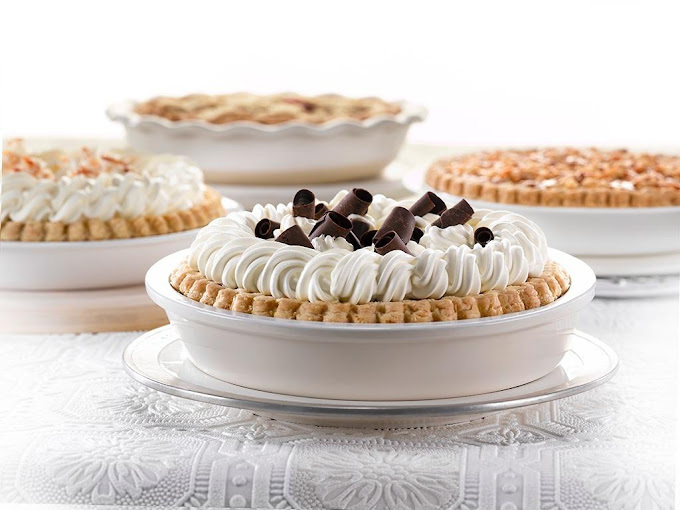 Light and airy photo of a pie with white frosting and chocolate shreds on a clear platter. The background features three similar pies.