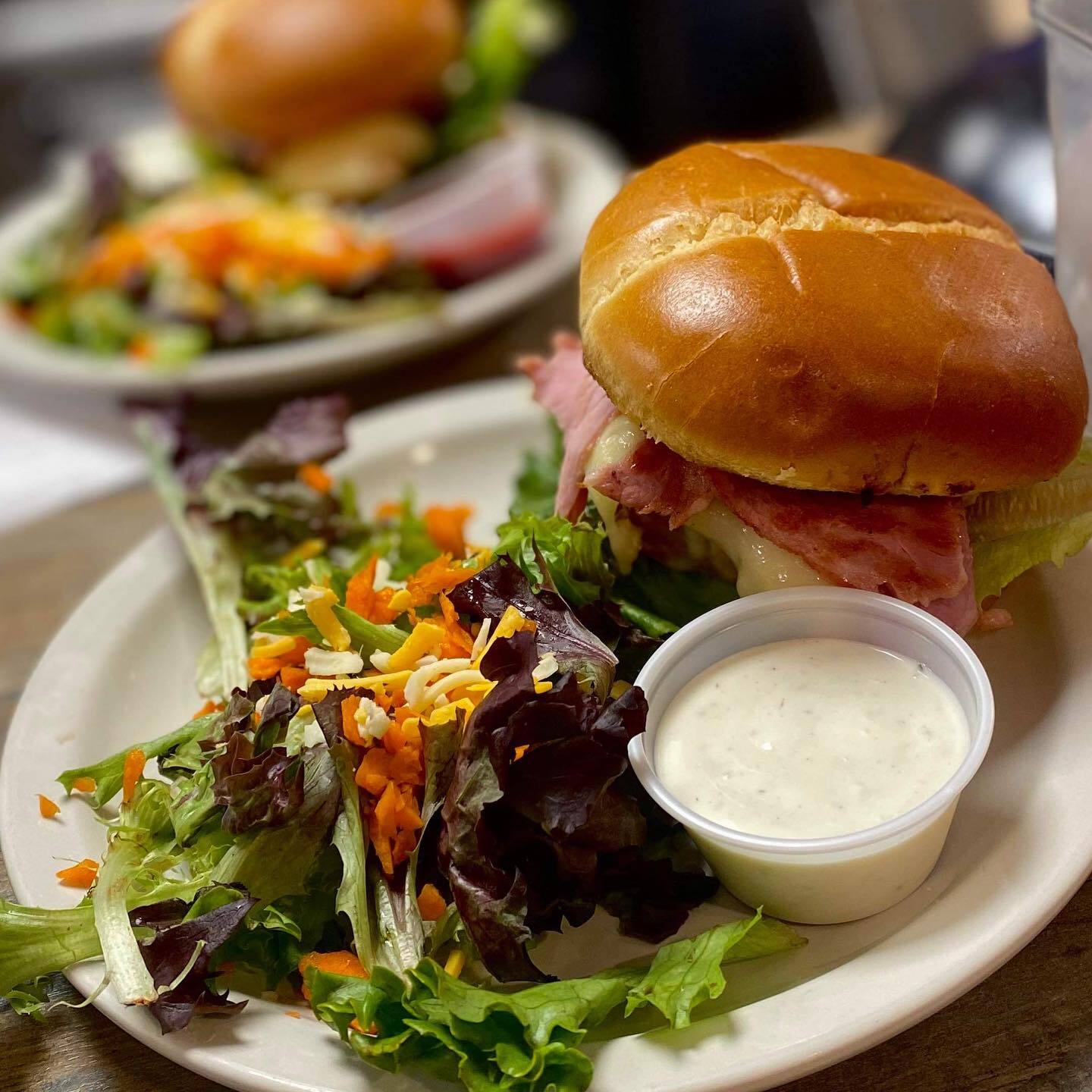 A burger, salad, and cup of ranch on a white plate.