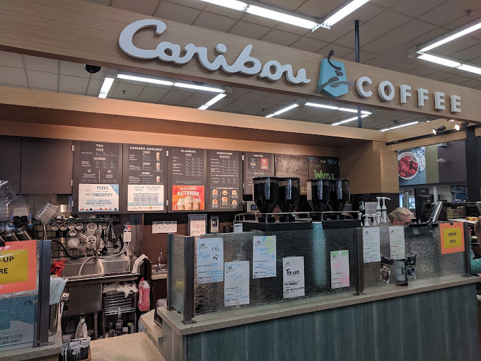 Interior view of the Caribou Coffee register. The back has menu signs and a sink. There are notes posted along the front divider of the table.