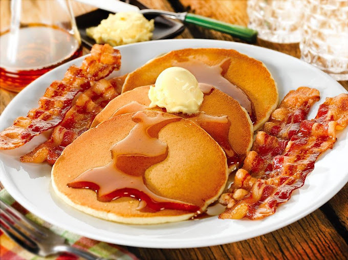 Plate of pancakes with butter and syrup, as well as multiple strips of bacon.