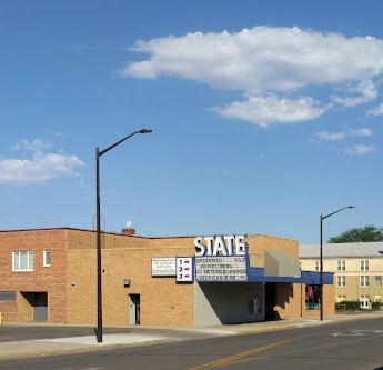 Exterior view of a blocky brown building. There are two light poles on either side of the building. The front entrance says "state" in big white letters.
