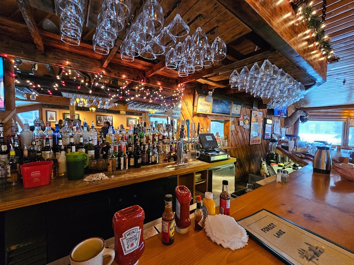 An inside view of a bar with moody lighting and various glasses lining above the bar.