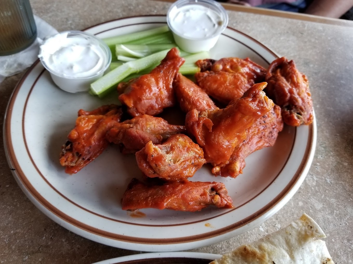 A white plate of wings with celery and two sides of ranch.