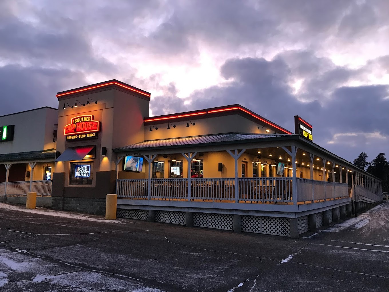 An outside view of an building at night, with a wrap around porch around the whole building and a red lighted sign above the porch and awning.