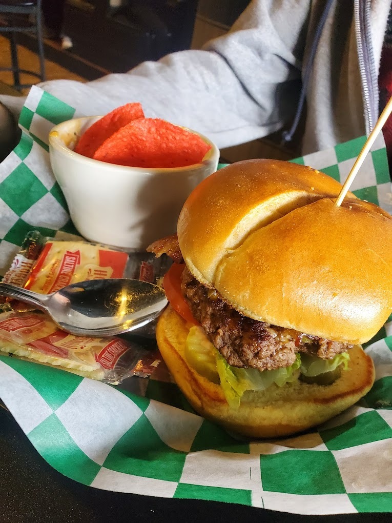 A food basket with a burger held together with a tooth pick, served with lettuce, a side of toast and a side bowl of watermelon.