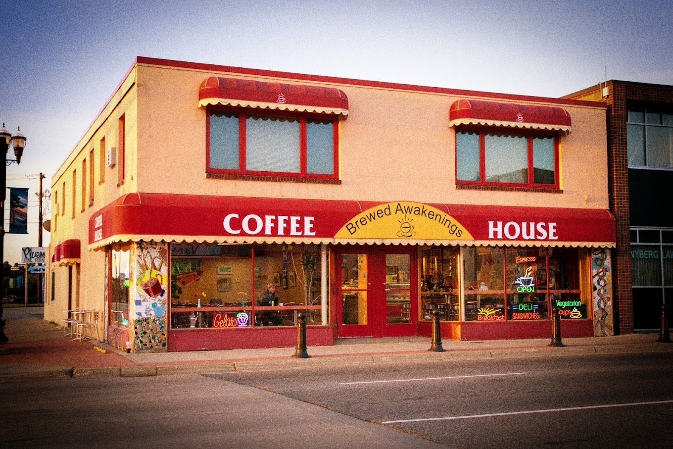 An outside view of an coffeehouse with light yellow exterior along with red awnings along the whole first floor above the windows and doors.