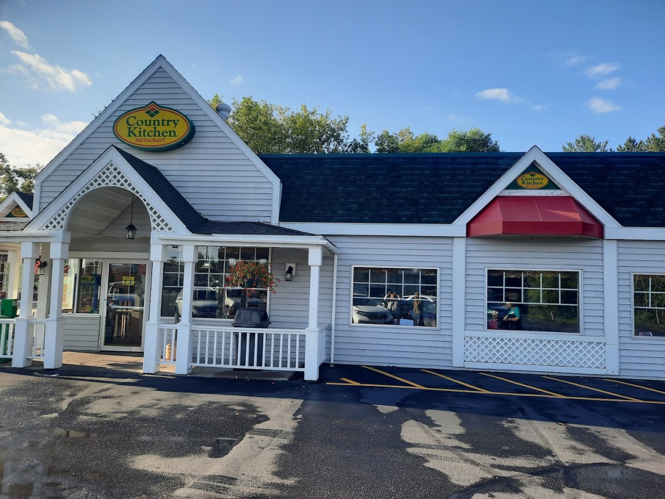 A white homey-style restaurant with an porch awning with a yellow sign right above the entrance.