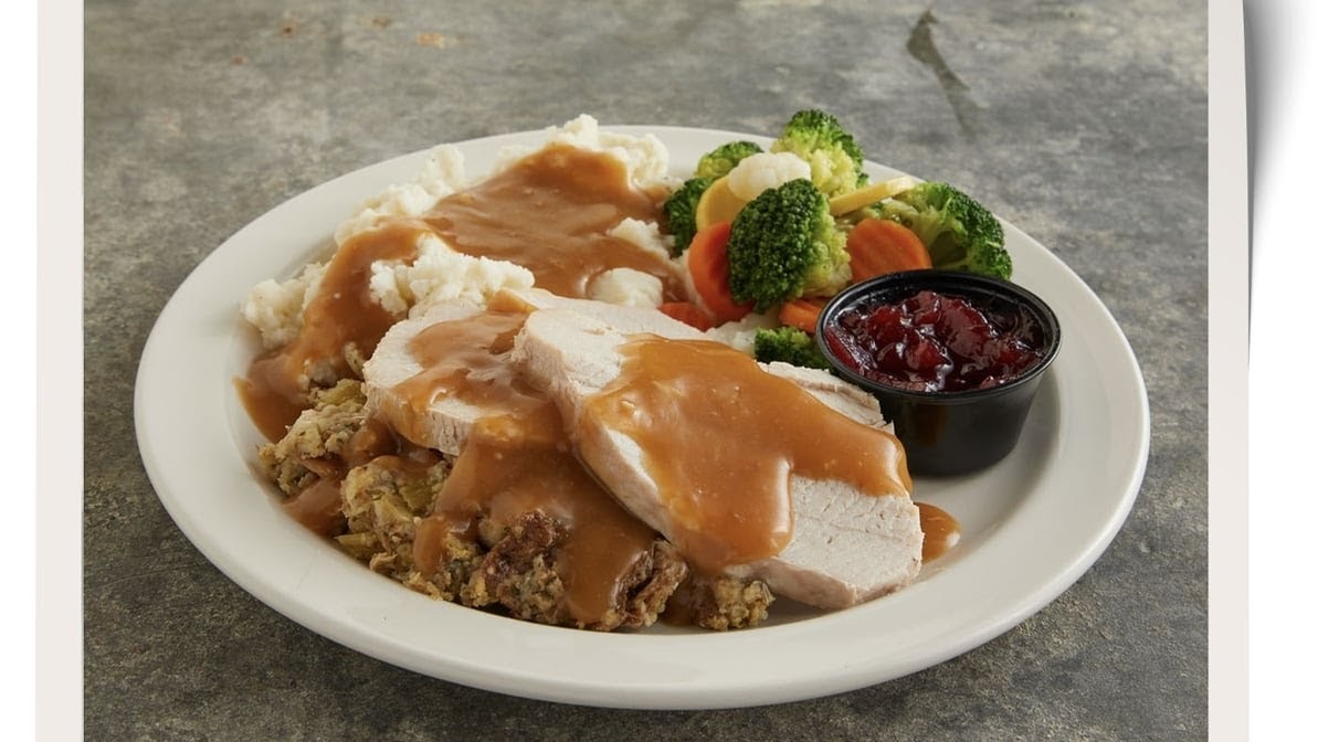 A white plate consisting of stuffing, cooked turkey, vegetables and mashed potatoes topped with gravy.