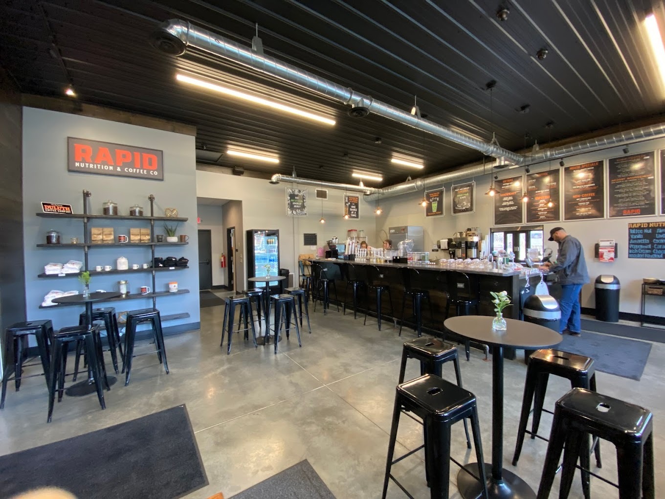 A view of a shop with a counter and coolers, chairs and tables in seating area.