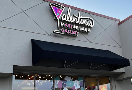 Upward view of a grey building. A neon logo stating "Valentini's Martini Bar and Gallery" is at the top of the building. Underneath is a black canopy and glass doors.