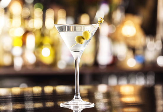 Close view of a light colored alcoholic drink with olives.