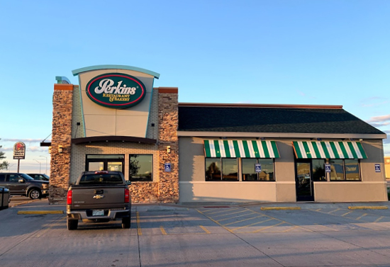 Outside view of the front of the Perkins building. It is brown with some brick detailing with green and white window canopies. A pickup truck blocks the view of the front doors.