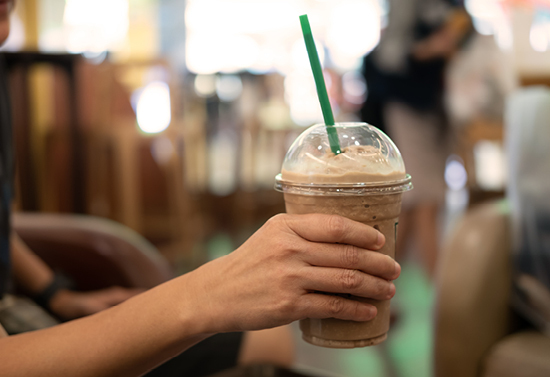 Hand holding an iced drink with a green straw.
