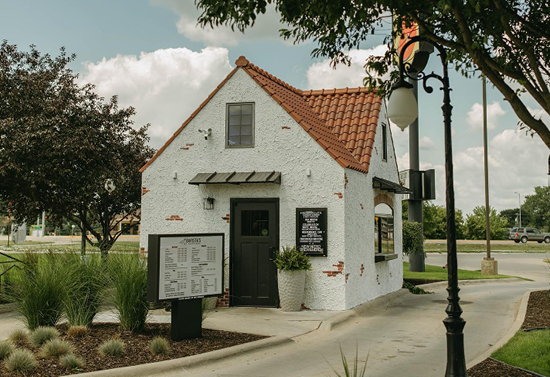 Cozy white building with orange roofing. There is a drive through sign and path beside it.