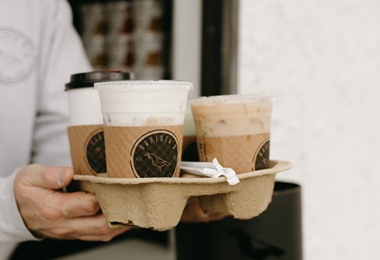 Close view of a man holding a carton of four different coffee drinks and straws.