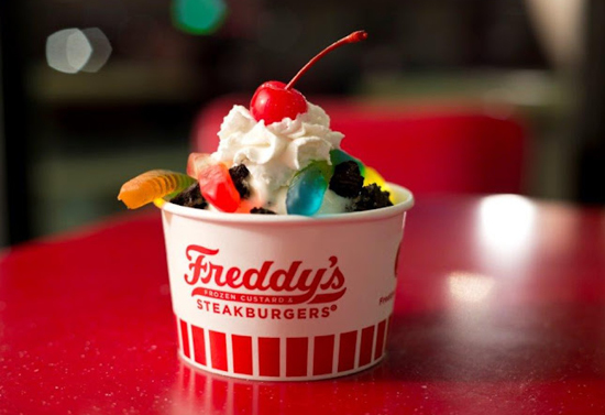 Ice cream with gummies, whipped cream, and a cherry in a red and white "Freddy's" container.