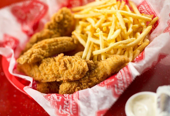 Close view of chicken nuggets and crispy fries in a red and white paper basket.