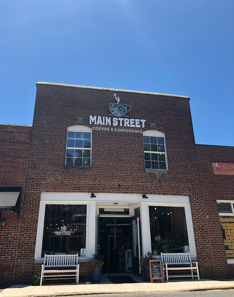 A brick building on main street with white trimming on the door and windows. A white sign above the door and windows reads "Main Street Coffee and Coworking"