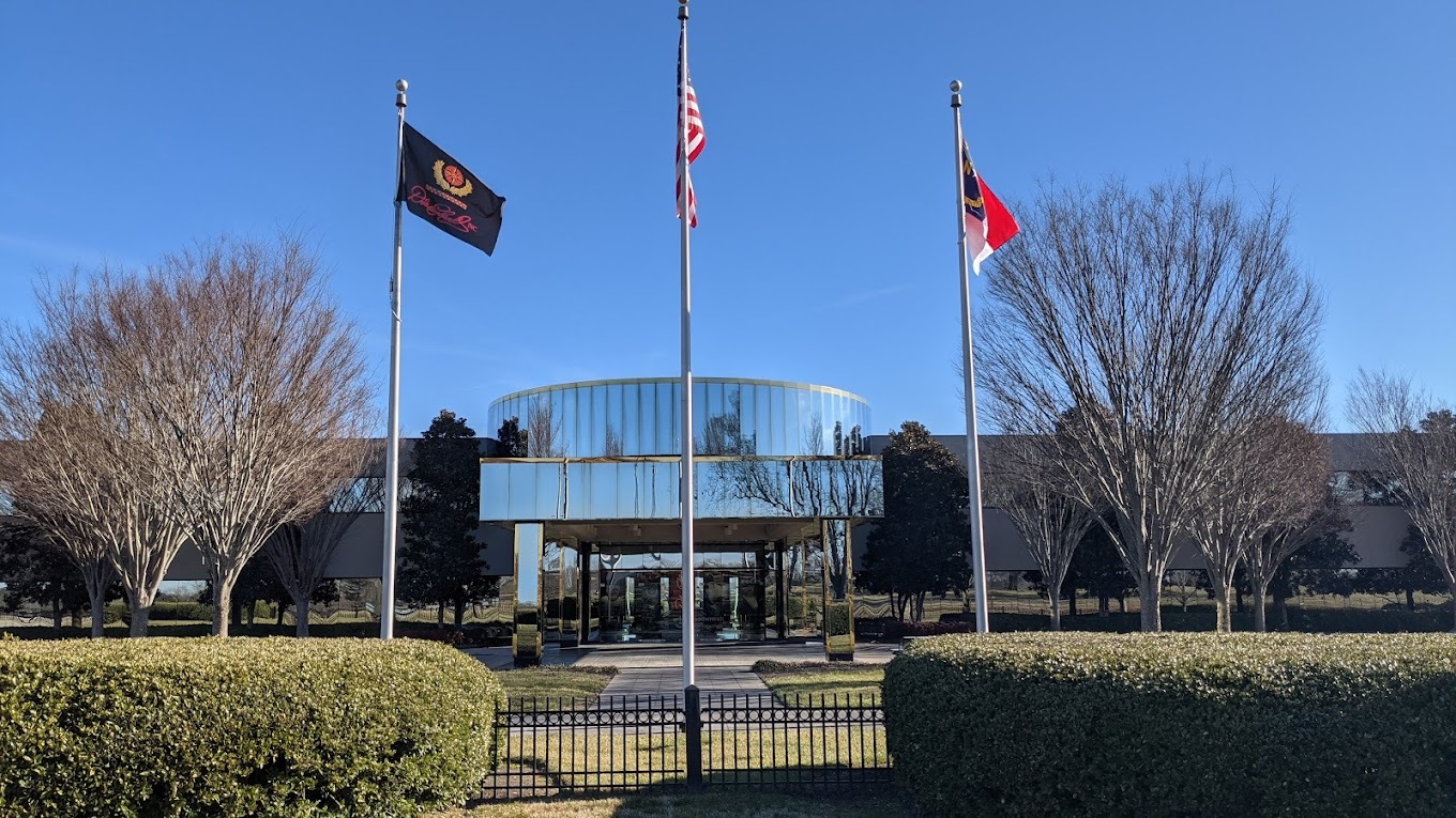 A view of a large building with a large front section made of glass with three flag poles sitting out front.