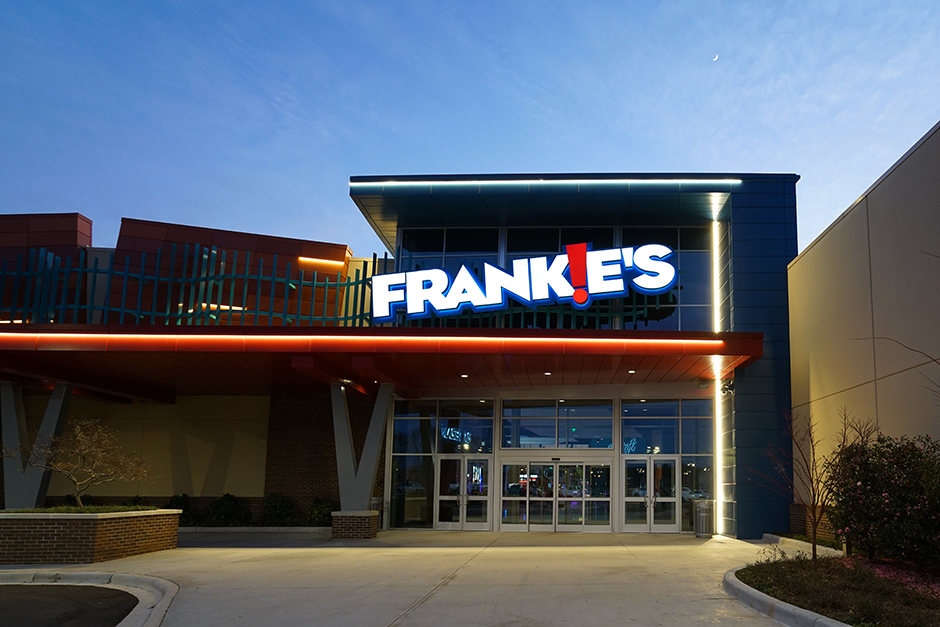 A outside view of a arcade called Frankie's, all lit up at with white and orange lights outside.