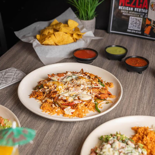 A white plate with rice topped with cheese and peppers, along with a side of tortilla chips, and three sides of sauces in black dishes off to the side.