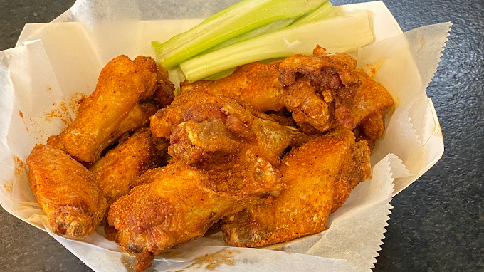 An view  of some chicken wings in a to-go carton with tissue and a side of celery.