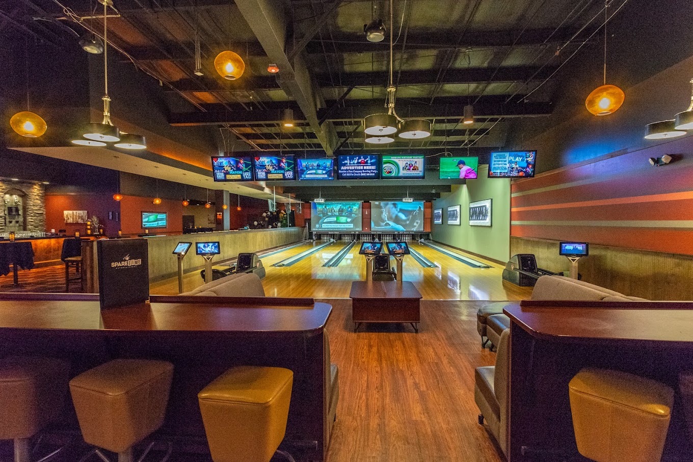 An view of bowling alley lanes with TVs lining the overhead of the lanes.