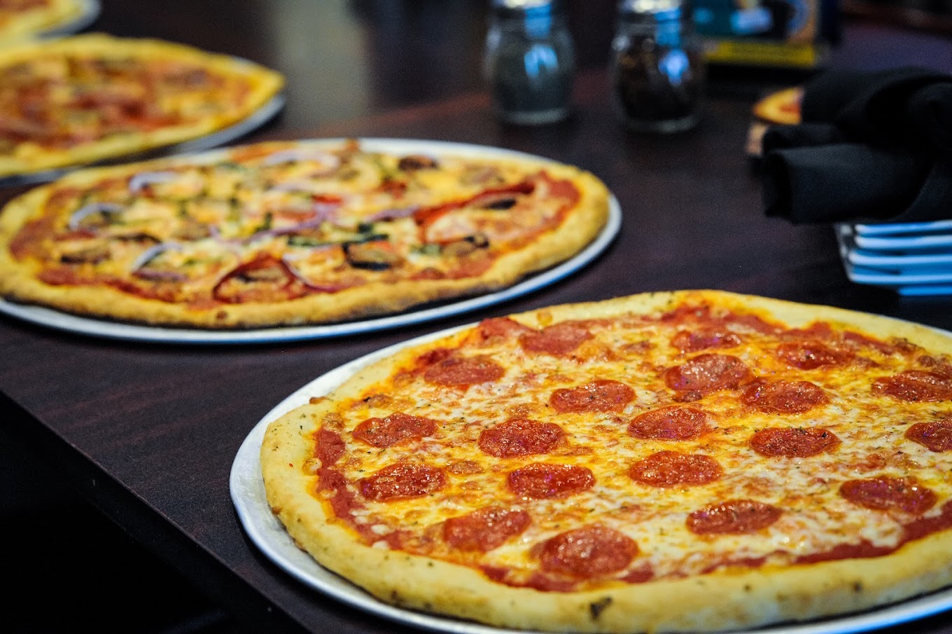 A view of three different kinds of pizzas, a pepperoni, veggie, and meat.