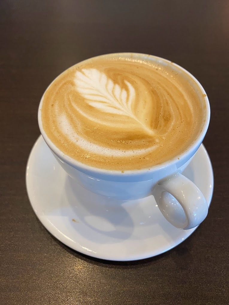 An view of a white coffee cup with an leaf latte art on the top.