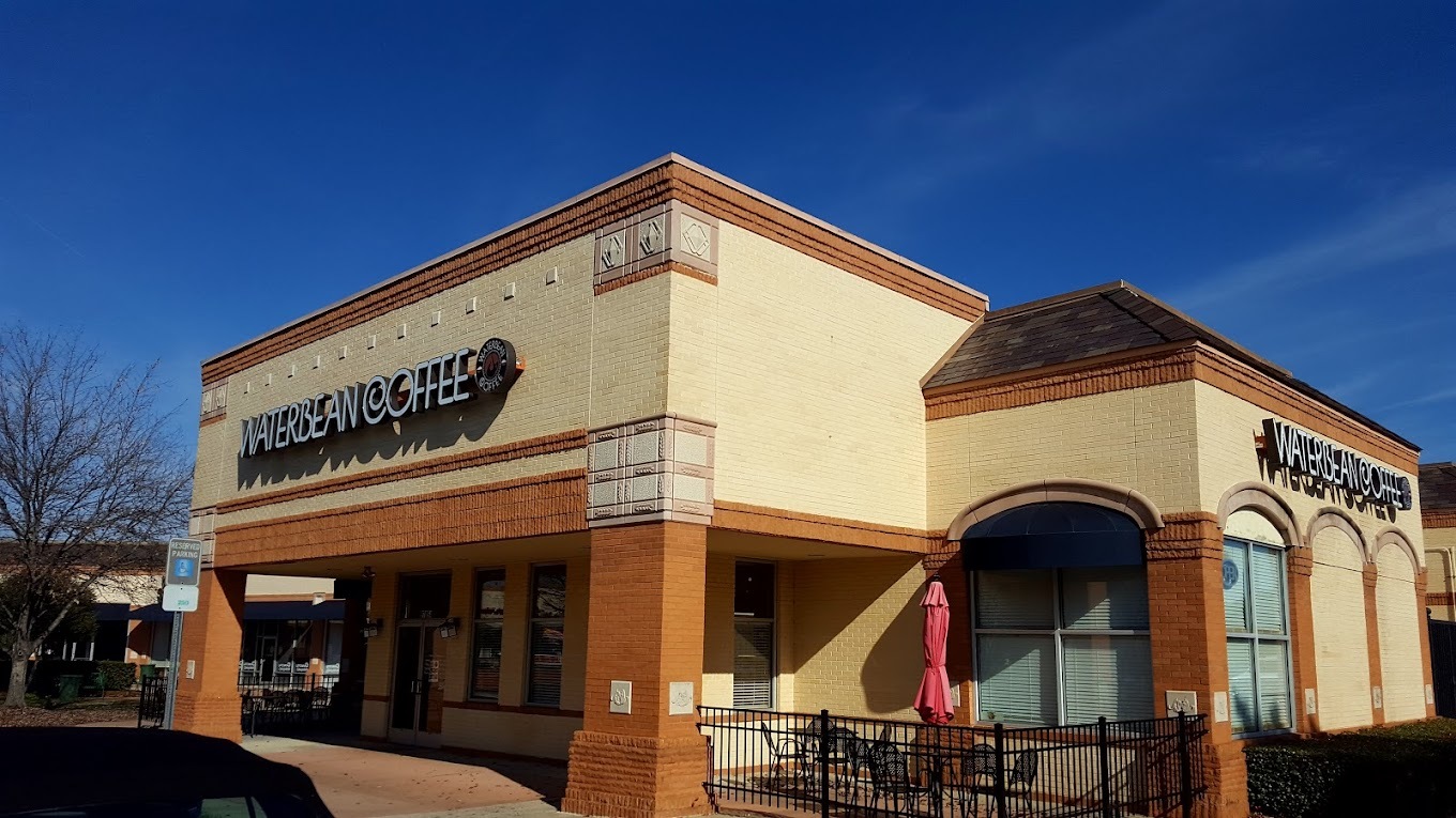 An outside view of a coffee shop, a large beige and orange-brown concrete building accompanied by a seating area outside of the building.