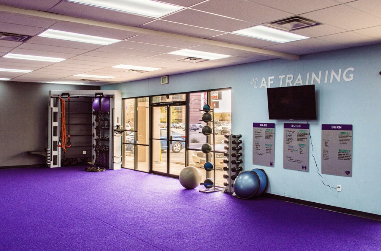 A room with purple carpet and blue walls, a tv is hung on the wall and workout balls are on the floor.