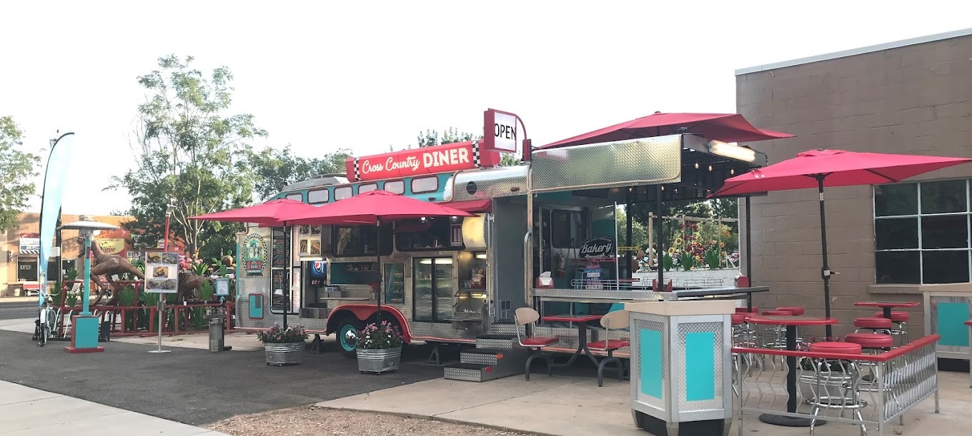 An outside view of a fancy food truck with a metal exterior, and lots of seating out front.