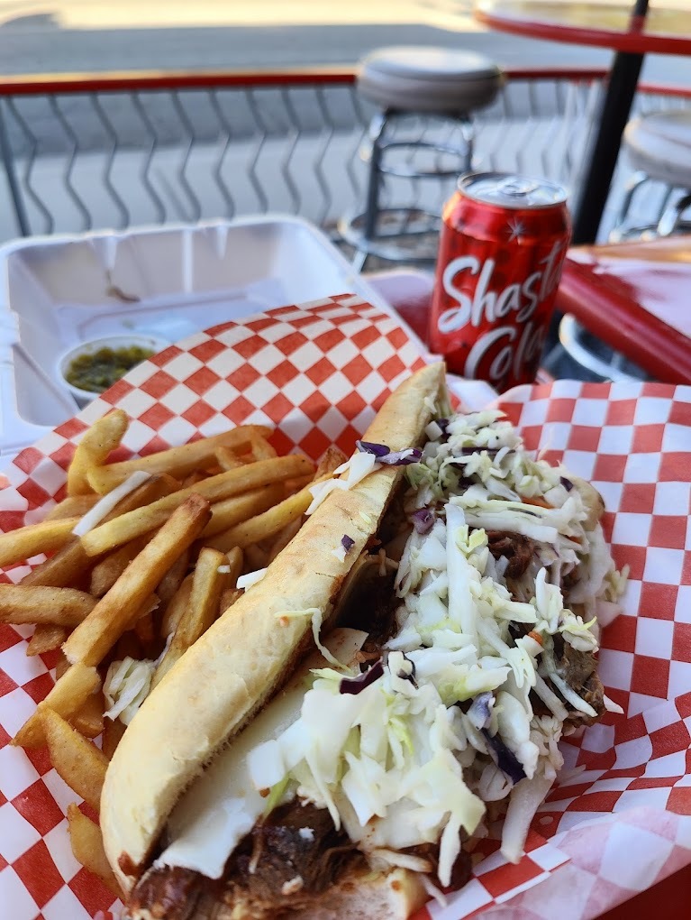 A view of a sandwich with a side of regular cut fries, set inside of a to-go box with red checkered paper.